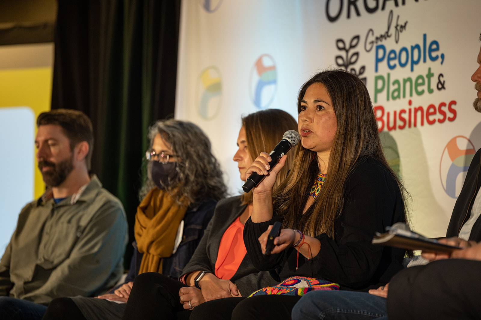 People in the stage and a woman speaking in the microphone